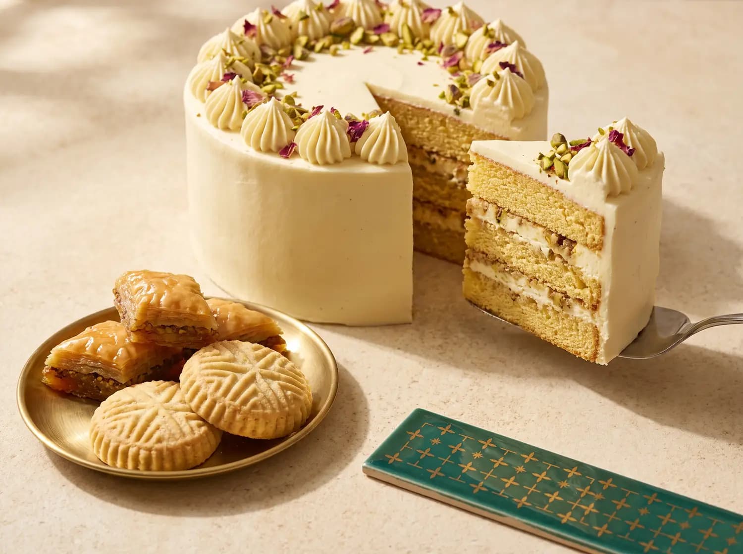 Symbolbild: eine angeschnittene Sahnetorte mit Pistazien und Rosenblüten, daneben Baklava und Mürbegebäck.